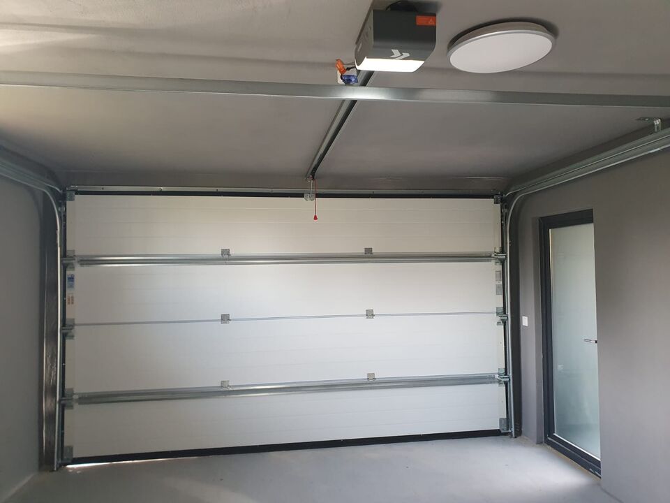 Ușă de garaj secțională văzută din interior, cu motor de acționare pe tavan și cordon de deblocare manuală