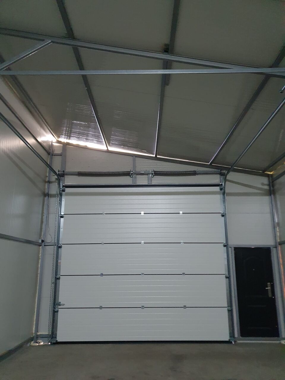 Interiorul unei clădiri pe structură metalică, cu ușă secțională, arcuri de torsiune și acționare cu lanț